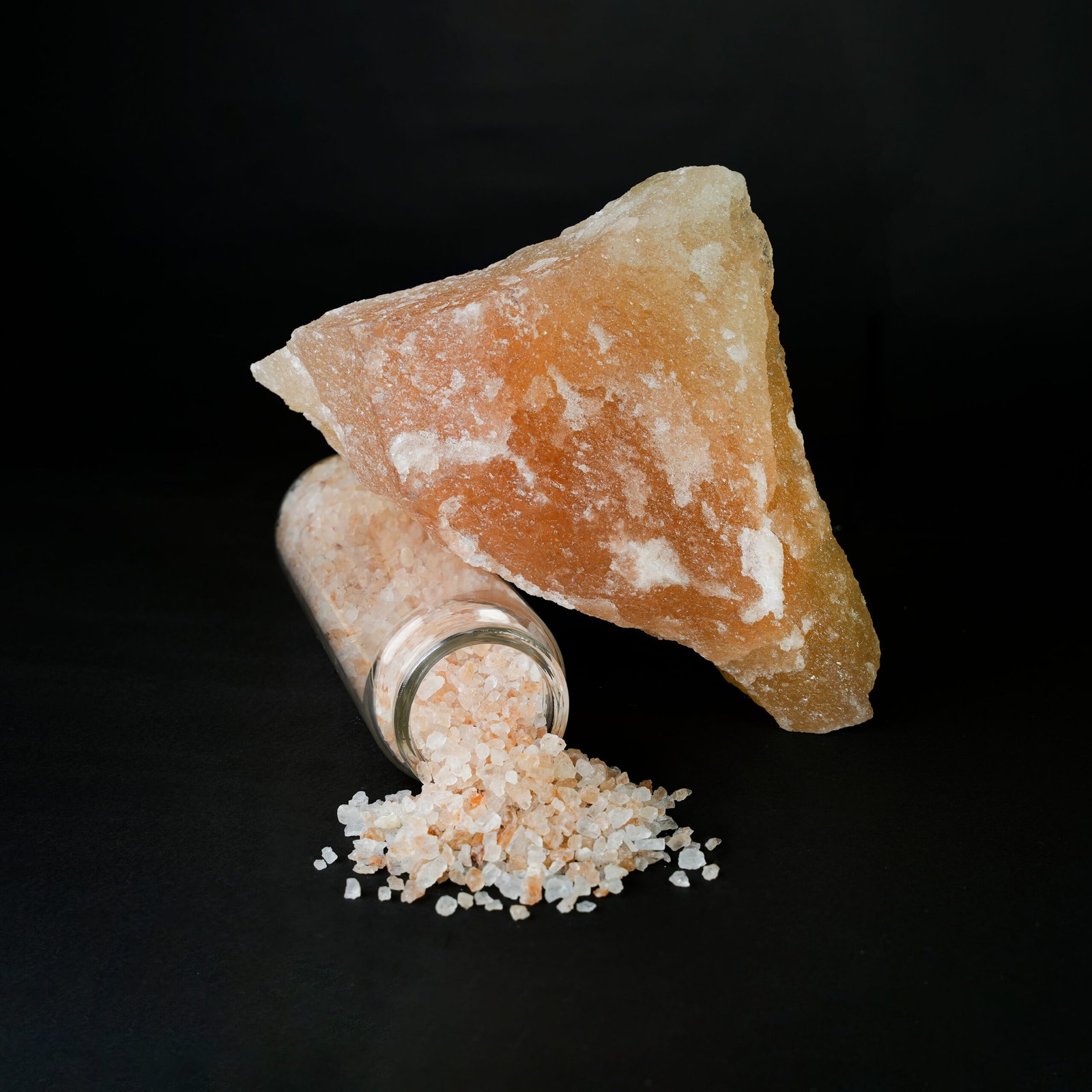 Natural orange-yellow mineral salt crystals stored in a clear glass jar, showcasing raw crystalline texture and warm mineral coloration